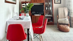 Un comedor con una mesa lista para dos personas, sillas rojas, un televisor y un aparador con puertas de cristal.