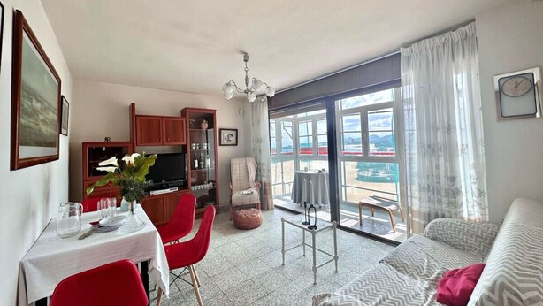 Una sala de estar con sofá, una mesa de comedor con sillas, una zona de cocina y un balcón con vistas.