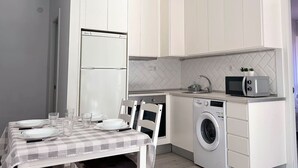 A compact kitchen with white cabinets, a built-in washing machine, a microwave, and a dining table set for four. - El Patuco - 30013 (Somo)