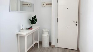 A white door with a handle, a white console table with a potted plant, a trash bin, and a mirror on the wall. - El Patuco - 30013 (Somo)