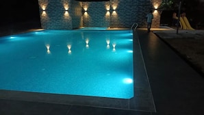 Una piscina con pared de piedra y luces, rodeada de una zona pavimentada.