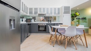 Una cocina moderna con armarios grises, un refrigerador de acero inoxidable y un comedor con sillas blancas y una mesa.