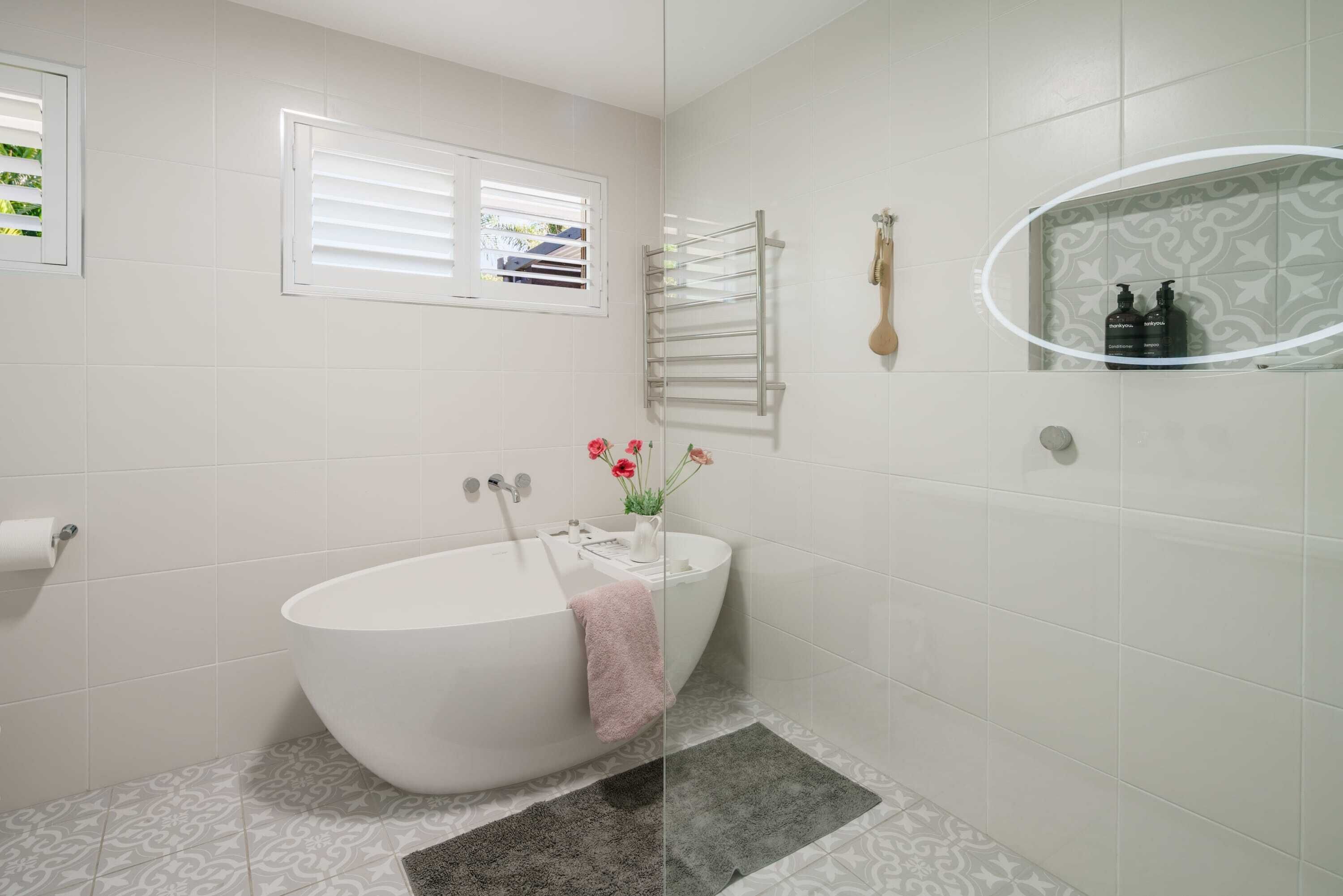 A modern bathroom with a freestanding bathtub, a toilet, a towel rack, and a mirror with a shelf.