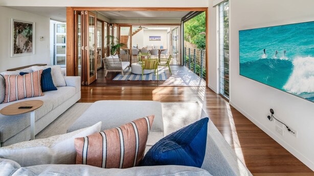 A modern living room with a sofa, a dining area, and a large window with a view of the outdoors. - Headlands Hideaway, Moffat Beach Dog Friendly Home (Caloundra Region)