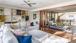 A modern living room with a sectional sofa, wooden flooring, and a dining area with chairs and a table. - Headlands Hideaway, Moffat Beach Dog Friendly Home (Caloundra Region)