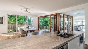 A modern kitchen with a marble countertop, a built-in dishwasher, and a sliding glass door leading to an outdoor area. - Headlands Hideaway, Moffat Beach Dog Friendly Home (Caloundra Region)