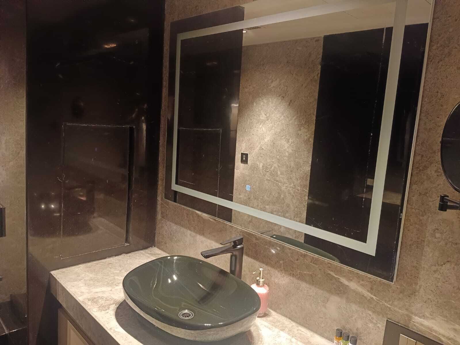 A modern bathroom with a large mirror, a glass vessel sink, and a marble countertop.