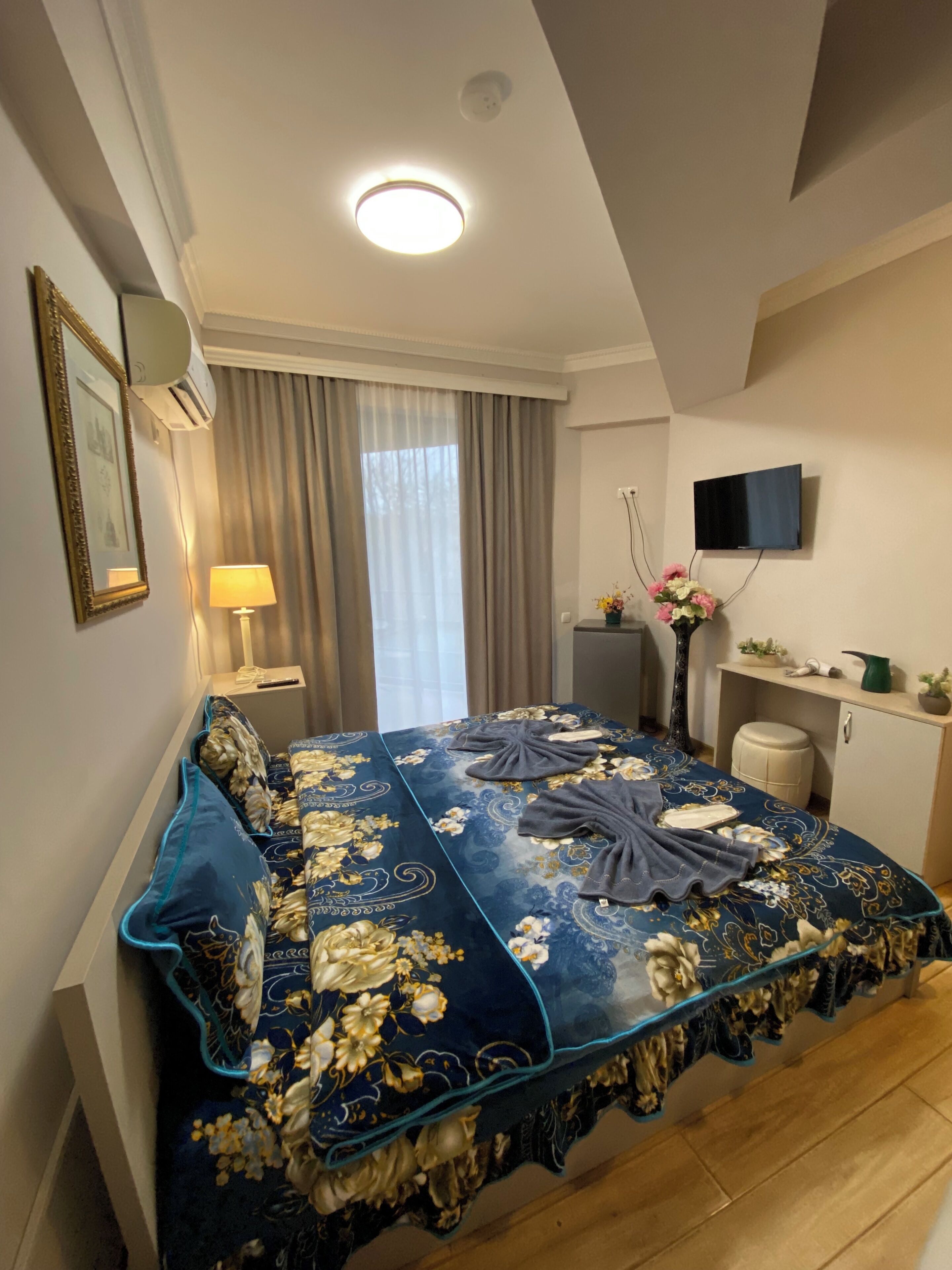 A bedroom with a bed, a TV, a desk, and a window with curtains.