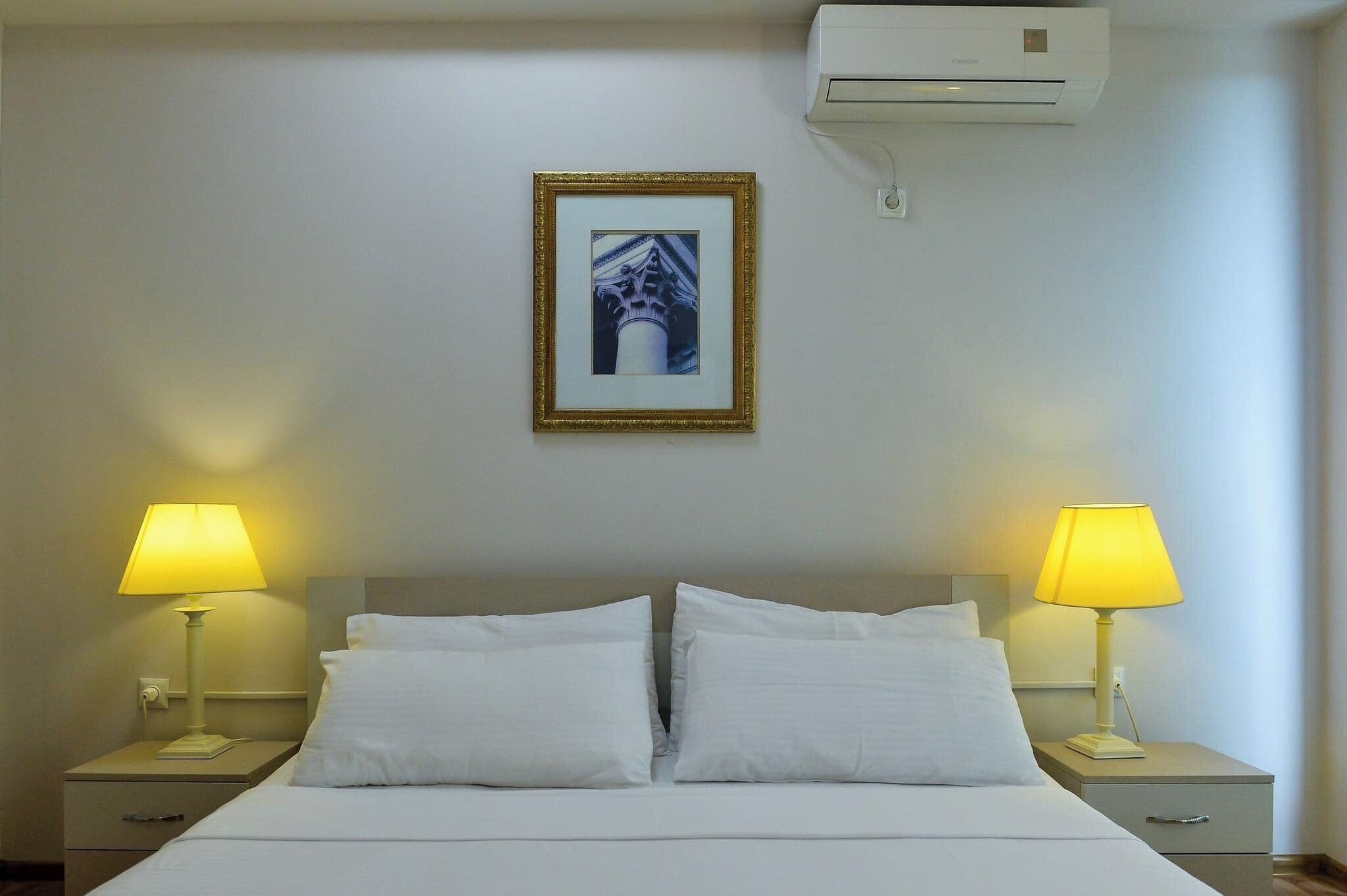 Hotelkamer met een bed, twee nachtkastjes met lampen, een lijst aan de muur en een airconditioner.