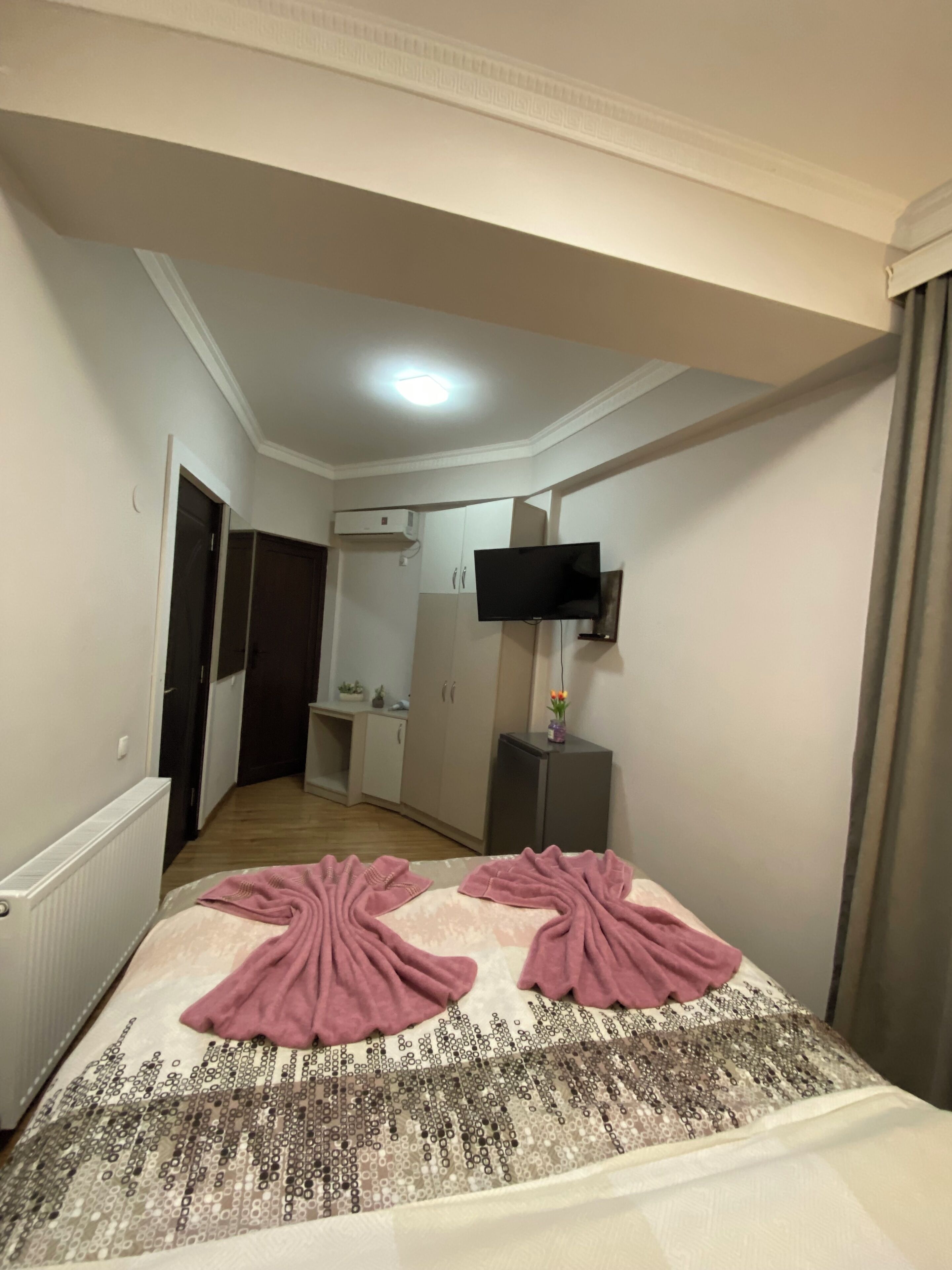 Una habitación de hotel con una cama, un televisor montado en la pared, una mesita de noche pequeña y una puerta que da a un baño.