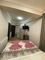 Une chambre d’hôtel avec un lit, un téléviseur fixé au mur, une petite table de chevet et une porte donnant sur une salle de bain.