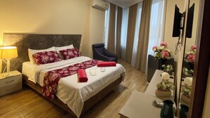 A hotel room with a bed, a chair, a desk, a mirror, and a window with curtains. - Grand Central (Tsqaltubo)