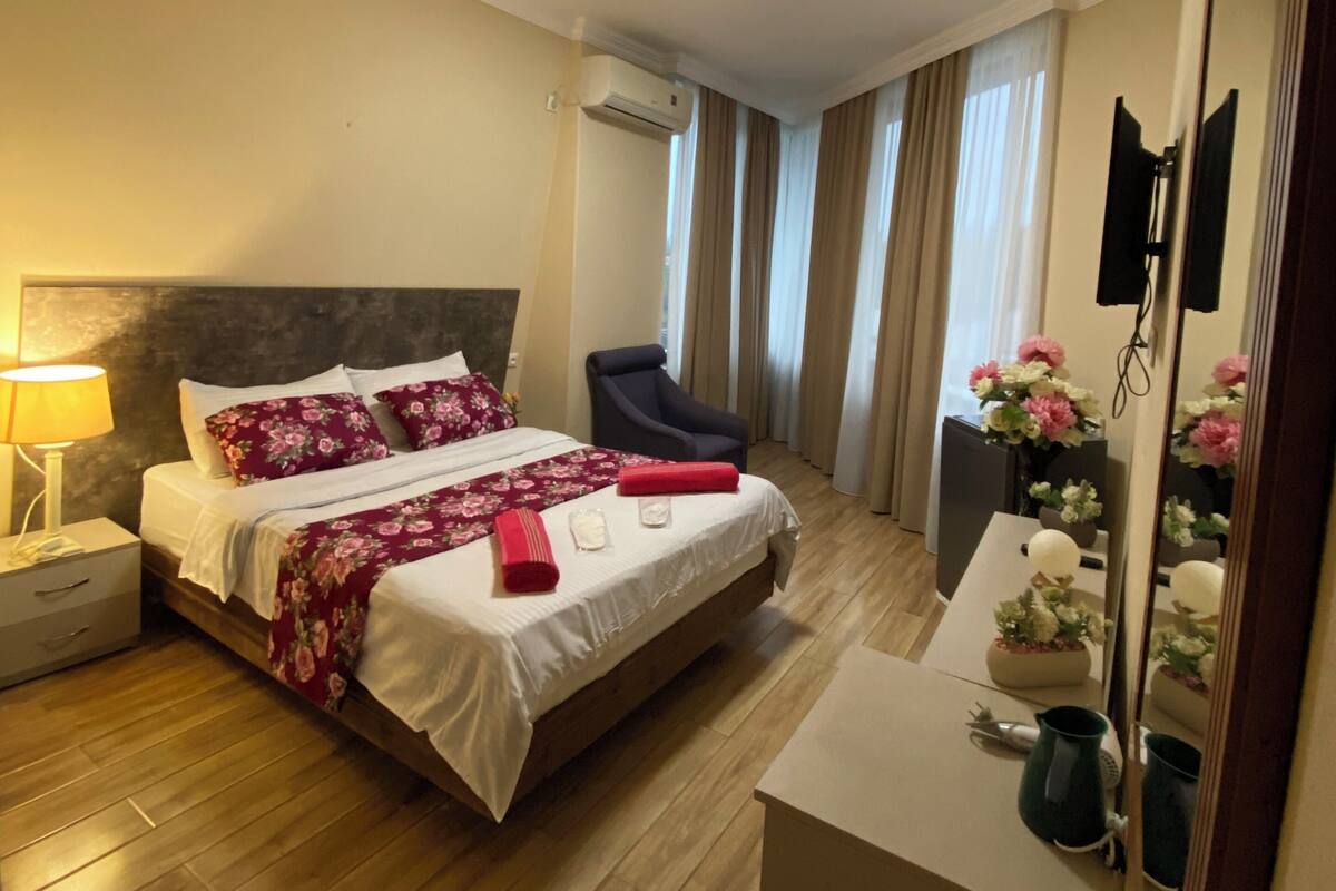 A hotel room with a bed, a chair, a desk, a mirror, and a window with curtains.