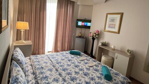 A hotel room with a bed, a desk, a TV, and a window with curtains. - Grand Central (Tsqaltubo)