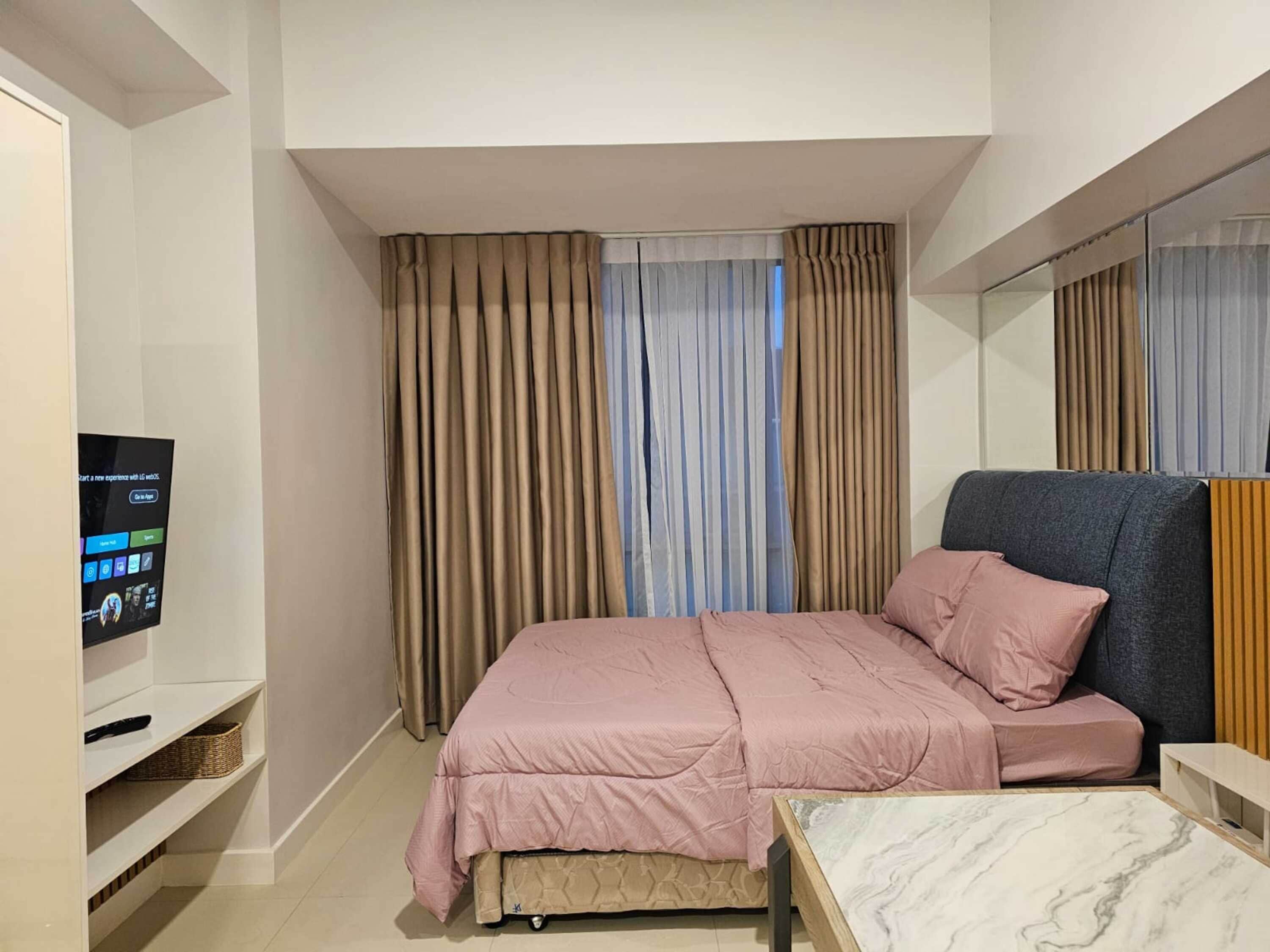 Une chambre à coucher moderne avec un lit, une télévision, une petite table et un miroir.