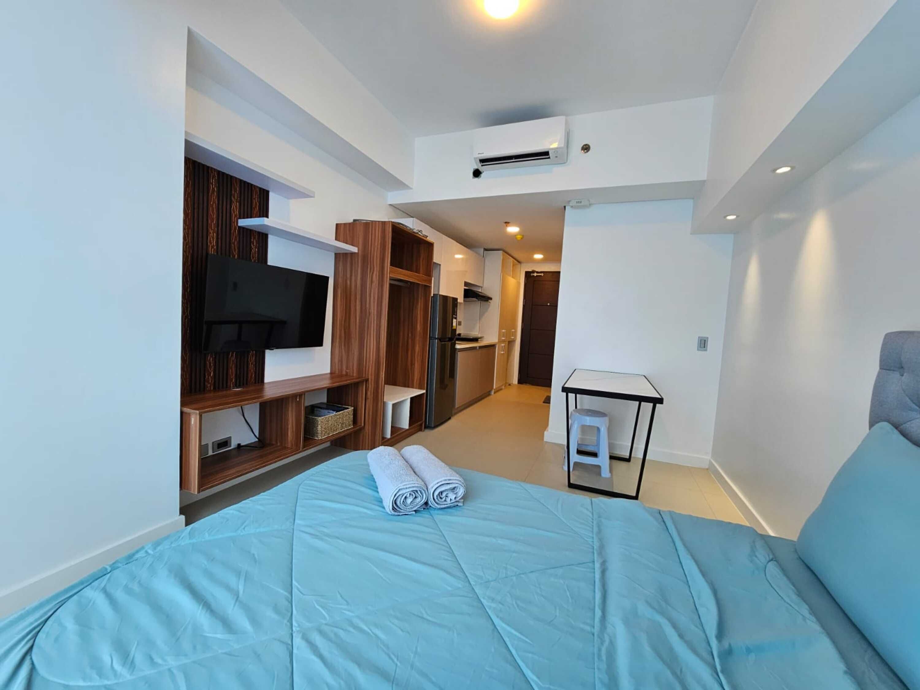 Une chambre d’hôtel moderne équipée d’un lit, d’une télévision, d’une kitchenette et d’une petite table.
