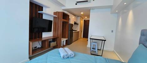Une chambre d’hôtel moderne équipée d’un lit, d’une télévision, d’une kitchenette et d’une petite table.
