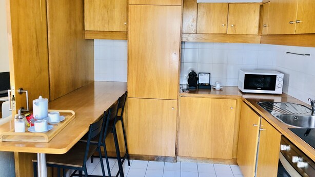 Een kleine keuken met houten kastjes, een magnetron, een koffiezetapparaat en een spoelbak.