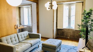 Een moderne woonkamer met een bank, voetenbankje en een grote potplant.