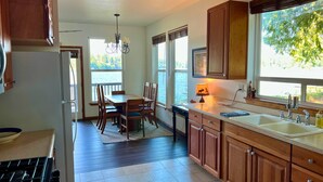 A kitchen with wooden cabinets, a dining table with chairs, a chandelier, and a view of the outdoors through large windows.