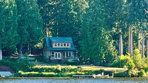 A house with a blue roof, surrounded by dense trees and a body of water.