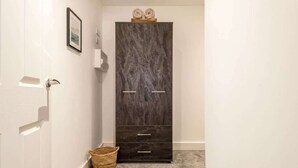 A hallway with a dark wooden wardrobe, a wicker basket, and a framed picture on the wall.