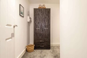 A hallway with a dark wooden wardrobe, a wicker basket, and a framed picture on the wall.