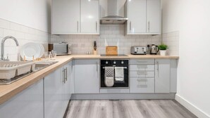 A modern kitchen with white cabinets, a built-in oven, a sink, and a countertop with various appliances.