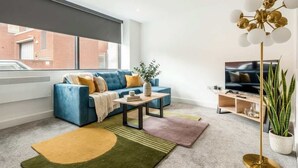 A modern living room with a blue sofa, a coffee table, a floor lamp, and a TV stand.