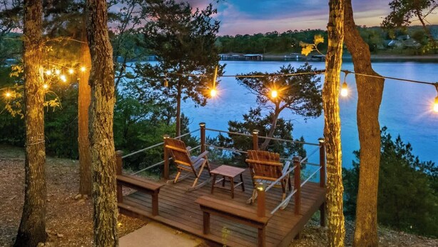 A wooden deck with chairs and tables, overlooking a body of water.