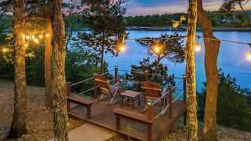 A wooden deck with chairs and tables, overlooking a body of water.