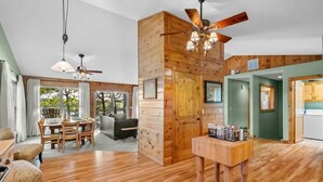 A spacious room with wooden floors, a dining area, a sofa, a ceiling fan, and a kitchen area.