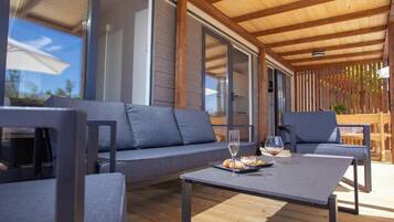 Un espacio al aire libre con piso de madera, sofás grises y una mesa con un vaso y comida.