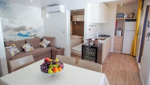 A compact living space with a kitchenette, a dining area with fruit, and a sofa with floral cushions. - Lastura Mobile Homes (Novalja)