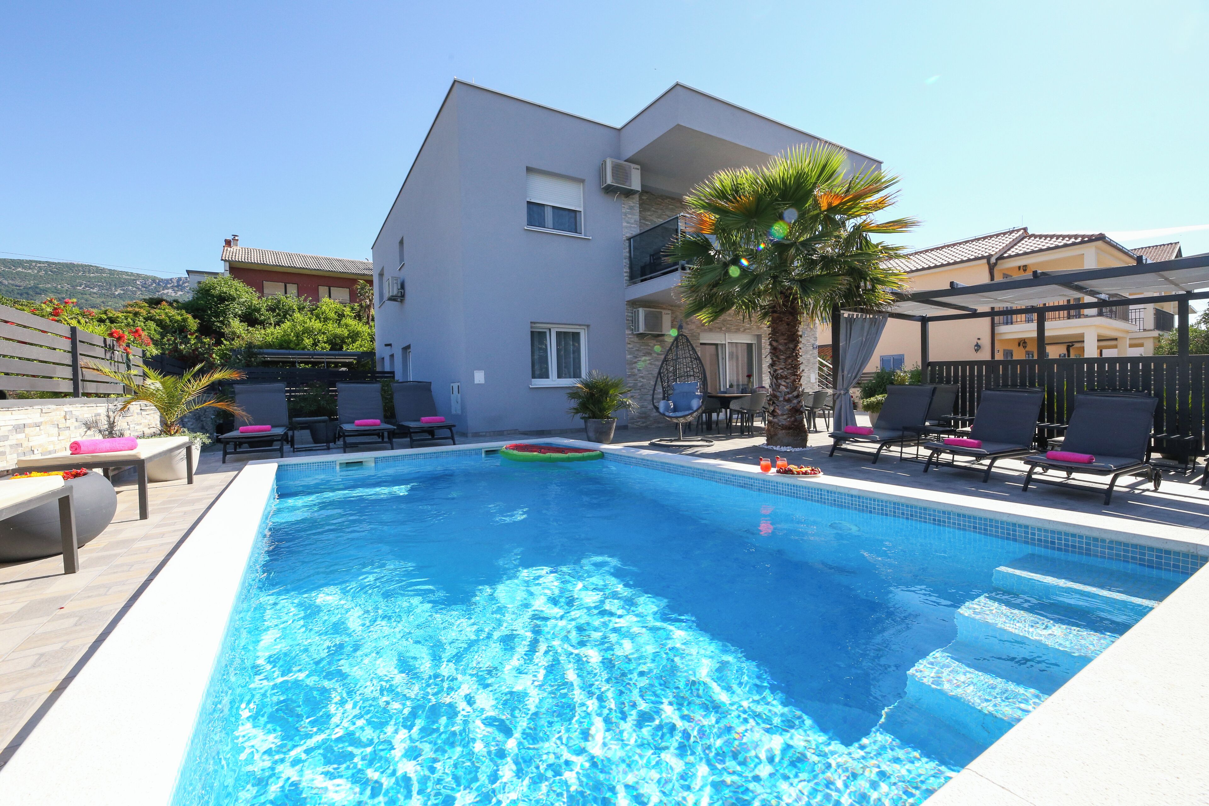 A swimming pool with lounge chairs and a palm tree, surrounded by buildings.