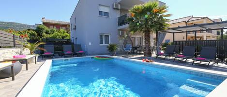 A swimming pool with lounge chairs and a palm tree, surrounded by buildings.