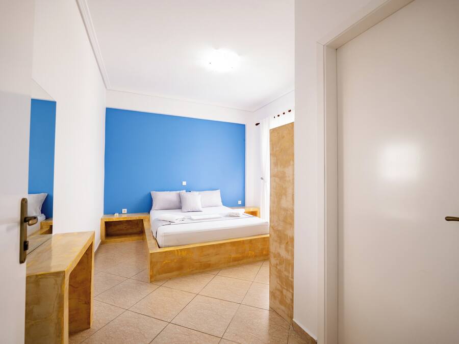 Una camera da letto con un letto, una panca in legno, un comodino e una porta.
