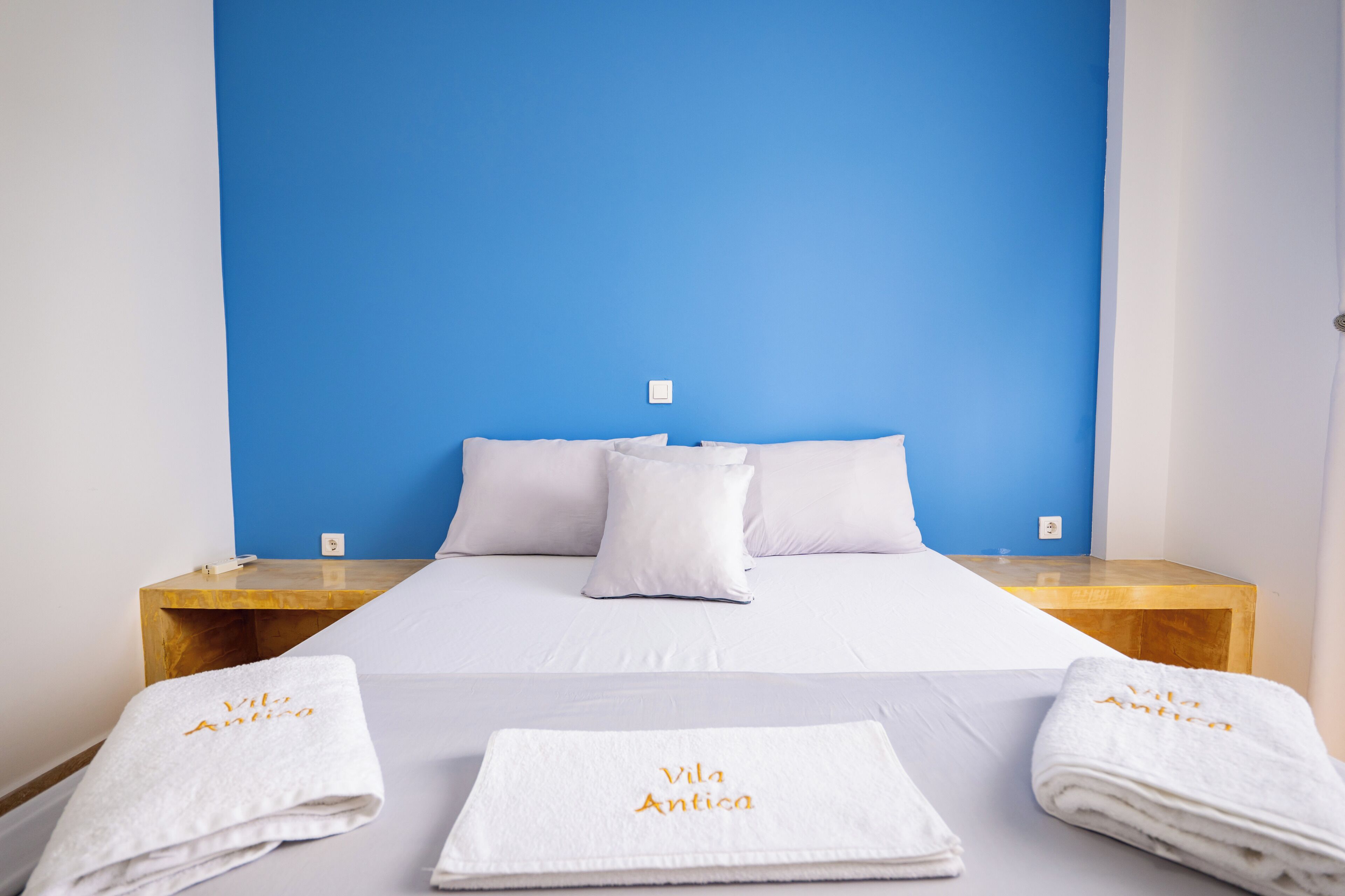 A hotel room with a bed, white linens, two nightstands, and a blue accent wall.