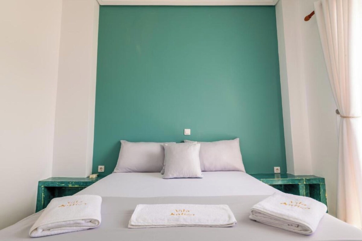 Una cama con ropa blanca, dos almohadas y una pared color turquesa.