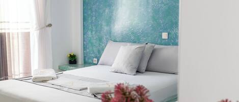 A bedroom with a bed, a nightstand, a vase with flowers, and a blue textured wall.