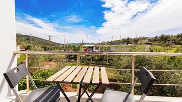 Un balcón con mesa de madera y dos sillas, con vistas a un paisaje rural con colinas y edificios dispersos.