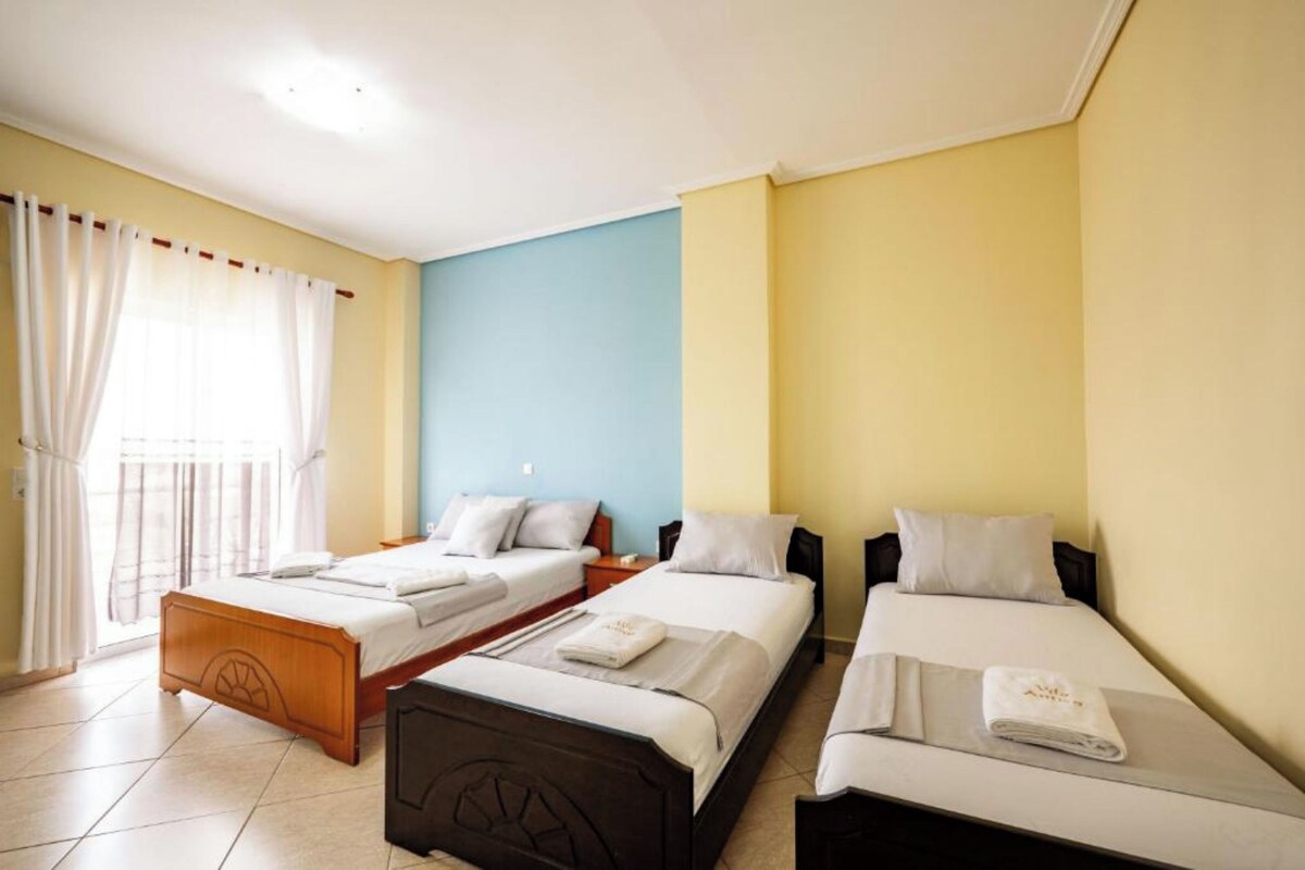 Habitación de hotel con dos camas individuales, cabecero de madera, pared azul decorativa y ventana con cortinas.