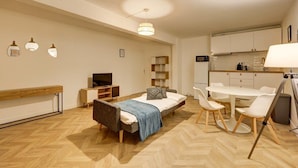 Ein modernes Schlafzimmer mit Bett, Nachttisch und Fernseher. Es gibt eine Küchenzeile mit Mikrowelle und einen Essbereich mit Tisch und Stühlen.