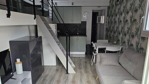 A modern living space with a staircase, grey sofa, and a kitchen area. - Quiet, small house in the hills above Toulon, close to all amenities. (LE REVEST LES EAUX)