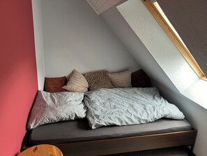 A corner bedroom with a sloped ceiling, a window, and a bed with patterned pillows.