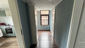 Ein Flur mit Holzboden, ein Fenster mit Aussicht und ein durchgehender Blick auf eine Küchenzeile.