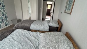 Ein Schlafzimmer mit zwei Betten, einem Holzkopfende, einer Deckenleuchte, einer Tür zu einem anderen Raum und einem gerahmten Bild an der Wand.
