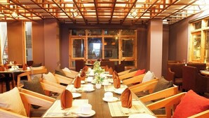 A restaurant with a long wooden table set for a meal, surrounded by wooden chairs with cushions.