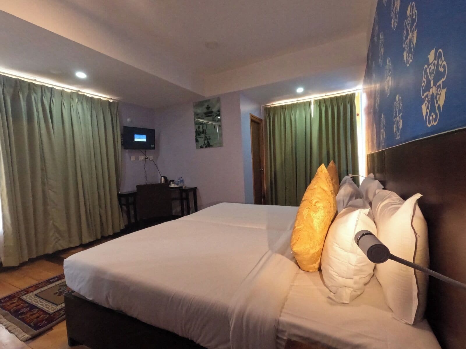 Een hotelkamer met een groot bed, een bureau met stoel, een televisie en groene gordijnen.