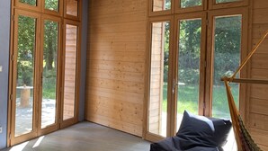 Een ruime kamer met grote ramen met houten kozijnen, een hangmat en een donkergroene bank.